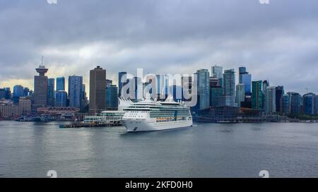 Ein Kreuzfahrtschiff verlässt den Kreuzfahrthafen und die Skyline der Stadt mit bewölktem Himmel im Hintergrund in Vancouver, Kanada Stockfoto