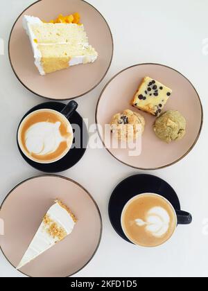 Minimalistisches Flatlay von zwei warmen Kaffees auf Tassen sowie Kuchen, Kekse und Brownies auf winzigen Tellern. Essen und Getränke auf einem weißen Tisch in einem Café im Freien. Stockfoto