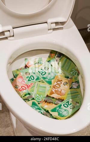 Kanadische zwanzig-, fünfzig- und einhundert-Dollar-Scheine in einer weißen Toilettenschüssel aus Porzellan. Stockfoto