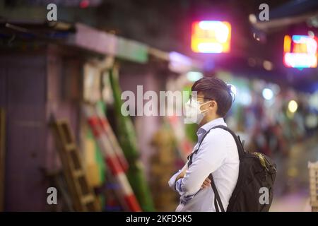 Ein Mann in einer Maske, der mit gekreuzten Armen auf den Straßen Hongkongs steht. Stockfoto