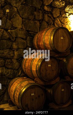 Eine vertikale Aufnahme von Weinfässern aus Holz in einem unterirdischen Keller gegen Steinmauer im Hintergrund Stockfoto