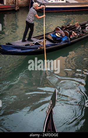 Gondoliere, die eine Gondel steuert, ein traditionelles venezianisches Ruderboot auf einem Kanal in Venedig, Italien Stockfoto