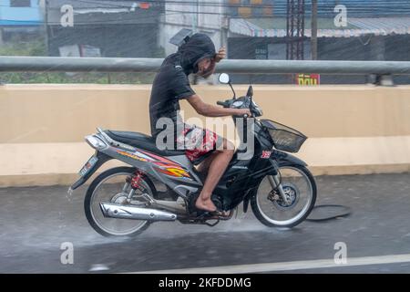 Ratchaburi, Thailand, 14 2022. NOVEMBER, Ein junger Mann fährt auf einem Motorrad und schützt seine Augen vor dem starken Regen mit seiner Hand Stockfoto