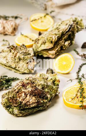 Frische pazifische Austern auf hellem Hintergrund. Zitrone und Orangano. Selektiver Fokus. Vertikale Aufnahme. Nahaufnahme Stockfoto