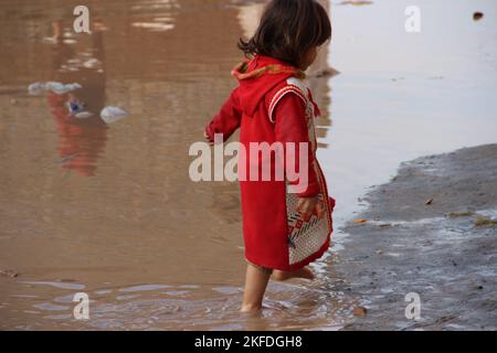 Kleines nettes Mädchen, springen im Wasser nach Regen, schlammiges Wasser.khyber Agentur, Peshawar, pakistan.april 2022. Stockfoto