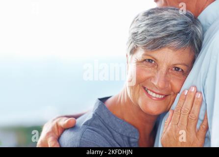 Reife Frau, die den Kopf auf der brust des mannes ruht. Porträt einer lächelnden reifen Frau, die sich im Freien mit dem Kopf gegen die brust von mans lehnt. Stockfoto