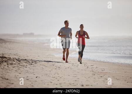 Ein frühes Joggen am Strand. Ein junges Paar trainiert im Freien. Stockfoto