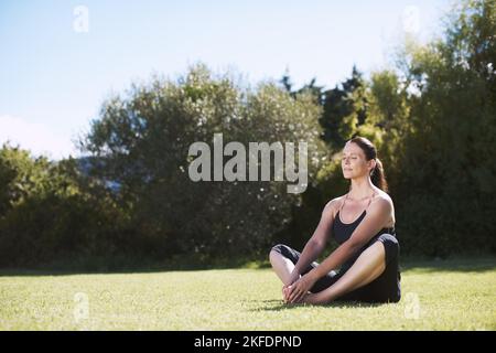 Die Bedeutung von Achtsamkeit. Eine attraktive Frau, die auf dem Gras sitzt und meditiert. Stockfoto