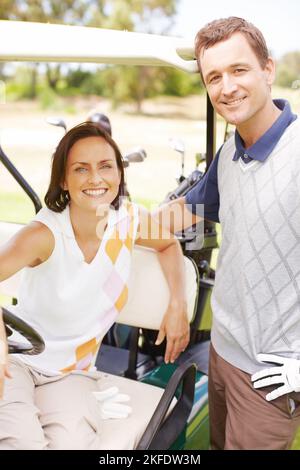 Ihre Liebe zum Golf brachte sie zusammen. Lächelnde Frau, die in einem Golfwagen saß und ihren Mann neben ihr stand. Stockfoto