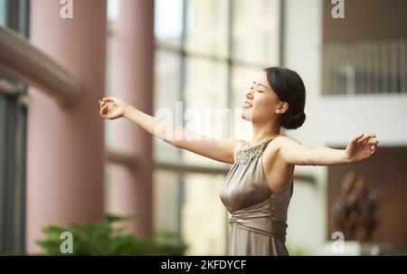 Umarmen Sie den Tag. Eine elegant gekleidete junge Frau, die durch einen großen Flur tanzt. Stockfoto