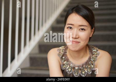 Strahlende Eleganz. Porträt einer elegant gekleideten jungen Frau, die auf einer Treppe sitzt. Stockfoto