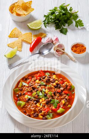 taco-Suppe aus Hackfleisch, Tomaten, gehackten grünen Chilis, Zwiebeln, Mais, Rote Bohnen und Taco-Würze in weißer Schale, vertikale Ansicht Stockfoto