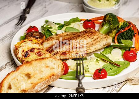 Fisch und Gemüse aus dem Meer. Tilapia-Filet mit Brokkoli, Kirschtomaten und Salat. Meeresfrüchte auf einem weißen Teller. Mediterranes Diät-Konzept Stockfoto