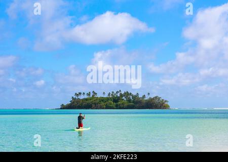 Ein Paddelboarder geht in Richtung einer kleinen tropischen Insel inmitten einer Lagune. Fotografiert in Muri Lagoon, Rarotonga, Cook Islands Stockfoto