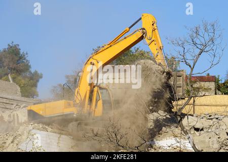 Yellow Raupenbagger zerstört baufällige Immobilien für den zukünftigen Bau eines modernen Hauses Stockfoto