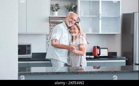 Liebe, Ehe und Tanz mit einem älteren Paar in der Küche ihres Hauses zusammen für die Bindung oder Romantik. Porträt, glücklich und lächeln mit einem reifen Stockfoto