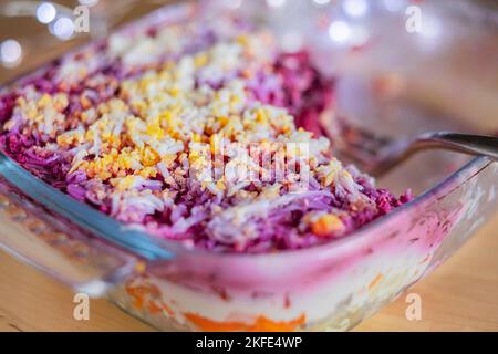 Mehrlagiger Salathering unter dem Pelzmantel auf dem Tisch. Portion von traditionellem russischen Salat mit Hering, Rüben, Karotten und Ei Stockfoto