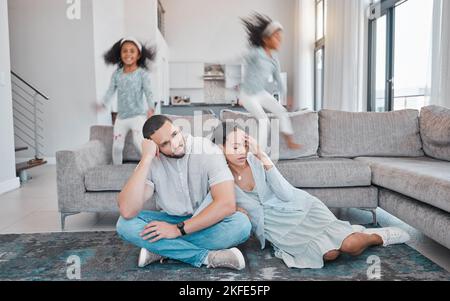Müde springen Eltern und Kinder auf das Sofa, während frustrierte Mama und Papa im Wohnzimmer auf dem Boden sitzen. Familie, erschöpftes Paar und verspielte Kinder mit Stockfoto