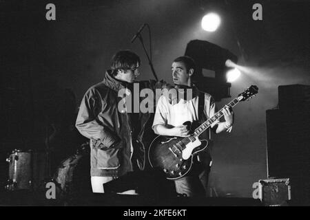 OASIS, FIRST GLASTONBURY HEADLINE, 1995: Liam Gallagher und Bonehead (Paul Arthurs) von Oasis teilen einen Moment während der Headline-Encore auf der Main Stage auf dem Höhepunkt ihres Ruhmes beim Glastonbury Festival, Pilton Farm, Somerset, England, 24. Juni 1995. 1995 feierte das Festival sein 25-jähriges Bestehen. In diesem Jahr gab es keine Pyramidenphase, da sie abgebrannt war. Foto: ROB WATKINS Stockfoto