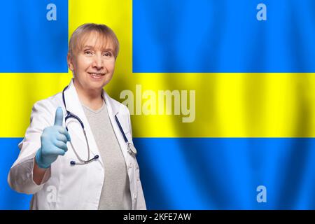 Schwedische lächelnde reife Ärztin mit Stethoskop auf Flagge von Schweden Hintergrund Stockfoto