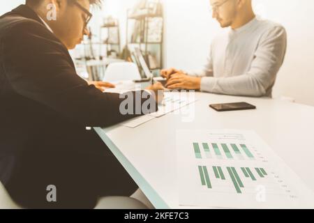 Junge Büroangestellte, die mit einem Computer am Schreibtisch sitzen. Zwei Geschäftsleute sprechen Stockfoto