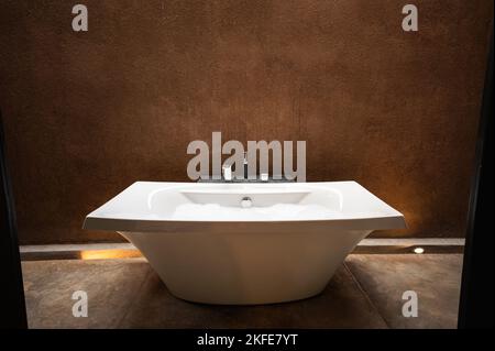 Elegante weiße Keramik-Badewanne mit Blase im Badezimmer in natürlichen Erdtönen Stockfoto