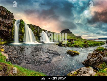 Fantastische Landschaft mit Sonnenuntergang über Kirkjufell Berg mit Kirkjufellsfoss Wasserfall und bunte Pileus Wolke im Sommer auf Island Stockfoto