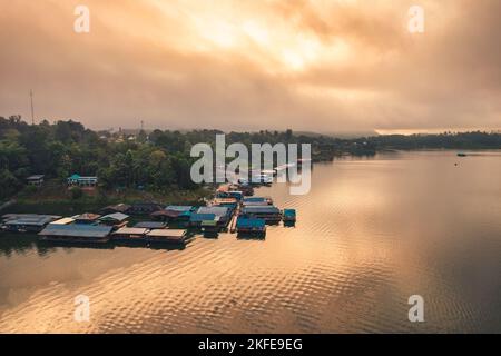 Landschaft mit goldenem Sonnenaufgang über dem lokalen traditionellen Dorf Mon, das am Morgen in Sangkhlaburi, Kanchanaburi, Thailand, mit Nebel im Damm schwimmt Stockfoto