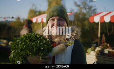 Erwachsene Frau posiert mit einer Tasche mit Obst oder Gemüse und schaut in die Kamera, kauft frische Produkte und kümmert sich um die Gesundheit. Einkaufen auf dem städtischen Bauernmarkt. Vegetarische und Bio-Lebensmittel. Hochformat. Stockfoto