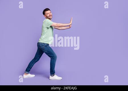 Foto in voller Größe von schönen jungen Mann schob leere Raum Wand fröhlich gekleidet stilvolle graue Kleidungsstück auf lila Hintergrund isoliert Stockfoto