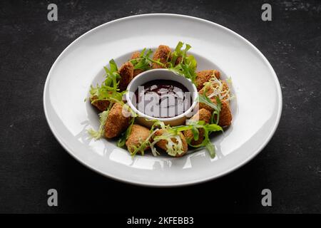 Käsenuggets mit Sauce auf einem Teller, auf dunklem Grund Stockfoto