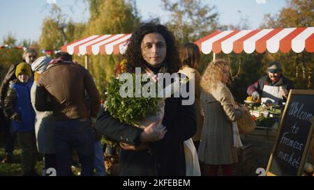 Der lockige Mann mittleren Alters posiert mit einer Tüte Gemüse oder Obst und schaut in die Kamera, kümmert sich um seine Gesundheit, indem er vegetarische, biologische und gesunde Produkte kauft. Stockfoto