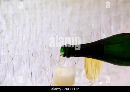 Nahaufnahme einer Champagnerflasche, die Champagner in eine Sektflöte vor einem verschwommenen Glas im Hintergrund pochelt Stockfoto