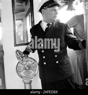 In der 1960s. Der Kapitän des Schiffes manövriert den Triebwerkstelegraphen, das Gerät, das auf einem Schiff verwendet wird, um den Techniker im Maschinenraum zu beordert, die Geschwindigkeit entweder rückwärts oder vorwärts zu erhöhen, anzuhalten oder im Stand zu sein. Das Bild wird aufgenommen, wenn der Kapitän des Schiffes den Telegrafen im Standby-Bereich hat und bereit ist, ihn zu wechseln. Das Schiff in der Waxholmsbolagets Flotte. Schweden 1964. Stockfoto