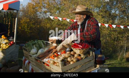 Der Bauer legt Obst oder Gemüse aus. Der Eigentümer der Verkaufsstelle teilt die Produkte mit dem Nachbarn. Der Senior fühlt sich glücklich, engagiert sich für die Lieblingsarbeit. Vegetarische und Bio-Lebensmittel. Landwirtschaft. Stockfoto