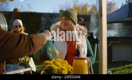 Erwachsene Frau wählt am Stand Äpfel mit Obst und Gemüse. Menschen, die im Hintergrund spazieren und einkaufen. Lokaler Bauernmarkt oder Fair im Freien. Vegetarische und Bio-Lebensmittel. Landwirtschaft. Stockfoto