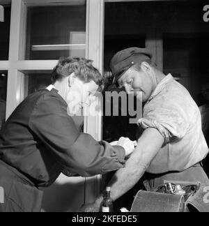 Impfstoff im Jahr 1950s. Krankenschwester Greta spritzt einen Impfstoff in den Arm eines Mannes in seiner Arbeitskleidung. Beide schauen auf den Arm und die Nadel, wenn die Impfung durchgeführt wird. Er scheint sich nicht um die Nadel zu kümmern. Im Jahr 1950s hatte die sehr schwere Krankheit Poliomyelitis, die häufig auf Polio verkürzt wurde, größere Ausbrüche, aber eine Impfung gegen sie, die vor einer Infektion durch das Virus geschützt war. Rimbo Schweden 1955 Stockfoto