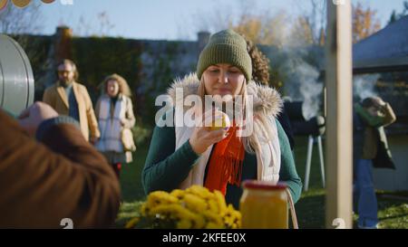 Erwachsene Frau wählt am Stand Äpfel mit Obst und Gemüse. Menschen, die im Hintergrund spazieren und einkaufen. Lokaler Bauernmarkt oder Fair im Freien. Vegetarische und Bio-Lebensmittel. Landwirtschaft. Stockfoto