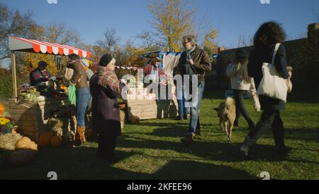 Viele verschiedene Menschen gehen, einkaufen, Obst und Gemüse auf dem lokalen Bauernmarkt auswählen. Herbstmesse am Wochenende im Freien. Vegetarische und Bio-Lebensmittel. Landwirtschaft. POS-System. Stockfoto