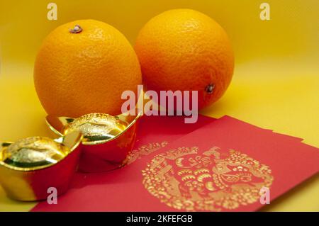 Chinesische Neujahrsdekoration mit Orangen, roten Päckchen und Goldbarren auf gelbem Deckgrund. Chinesisches Weihnachtskonzept. Stockfoto