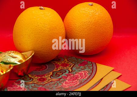 Chinesische Neujahrsdekoration mit Orangen, bunten Päckchen und Goldbarren auf rotem Cover-Hintergrund. Chinesisches Weihnachtskonzept Stockfoto