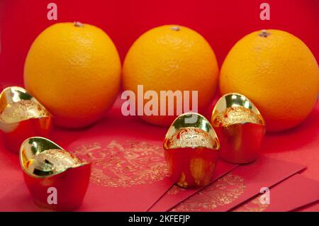 Chinesische Neujahrsdekoration mit Orangen, roten Päckchen und Goldbarren auf rotem Cover-Hintergrund. Chinesisches Weihnachtskonzept. Stockfoto