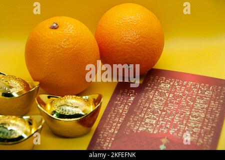 Chinesische Neujahrsdekoration mit Orangen, dunkelroten Päckchen und Goldbarren auf gelbem Deckgrund. Chinesisches Weihnachtskonzept. Stockfoto