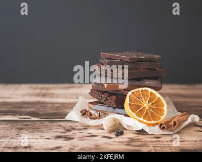 Haufen köstlicher dunkler und milchender Schokoladen-Riegel mit aromatischen Gewürzen auf Holzhintergrund, selektiver Fokus. Stillleben mit Schokoladenstücken, trockener Orang Stockfoto