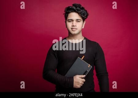 Junger gutaussehender indischer Mann, der ein Buch in einer ungezwungenen Umgebung hält Neugier, persönliche Interessen und Liebe zum Lernen, pädagogische Themen, Buchliebhaber Stockfoto