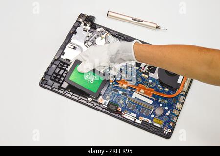 Foto eines Technikers, der eine 240-GB-ssd-Festplatte auf ein Notebook-Motherboard auf weißem Hintergrund einlegt. Stockfoto