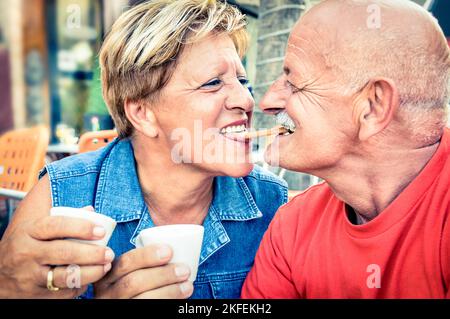 Glückliches verspieltes verliebtes Seniorenpaar, das zärtlich eine Tasse Kaffee genießt - fröhlicher älterer aktiver Lebensstil - Mann, der Spaß hat und mit ihrer Frau lächelt Stockfoto