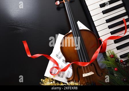 Musikalisches Veranstaltungskonzept Weihnachten mit Klavier und Geige auf schwarzem Holztisch mit Noten und Weihnachtsdekoration. Draufsicht. Stockfoto