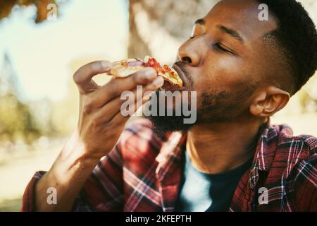 Fast Food, hungrig und schwarzer Mann essen Pizza für leckere und leckere Mittagspause im Park. Gen z, Essen und Hunger von jungen Menschen genießen Kohlenhydrate Pizza Stockfoto