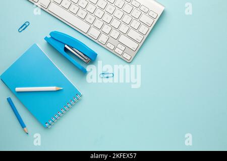 Blauer Arbeitstisch mit Tastatur, Notizbuch, Bleistift, Hefter und Büroklammern. Platz für Ihre Inschrift. Stockfoto